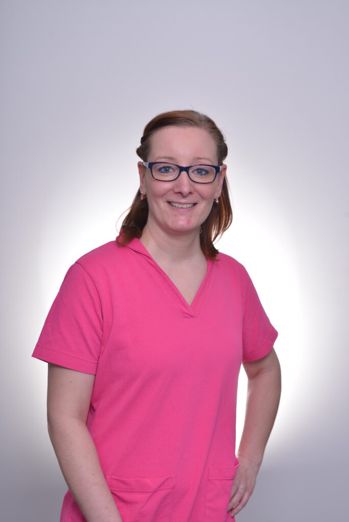 Mitarbeiterin in pinker Bluse vor neutralem Hintergrund