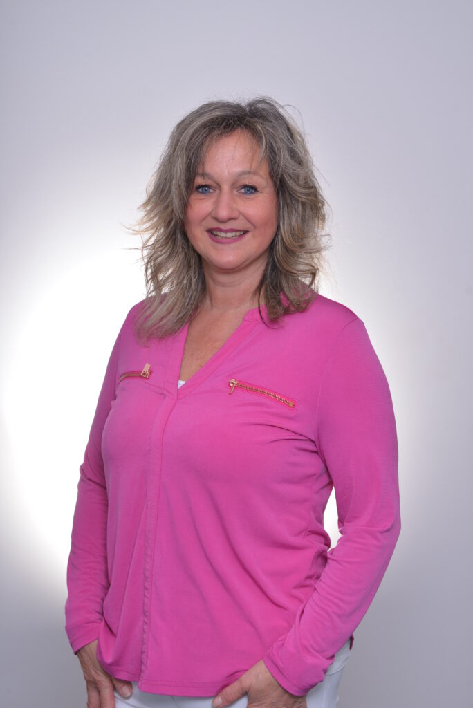 Mitarbeiterin in pinker Bluse vor neutralem Hintergrund.