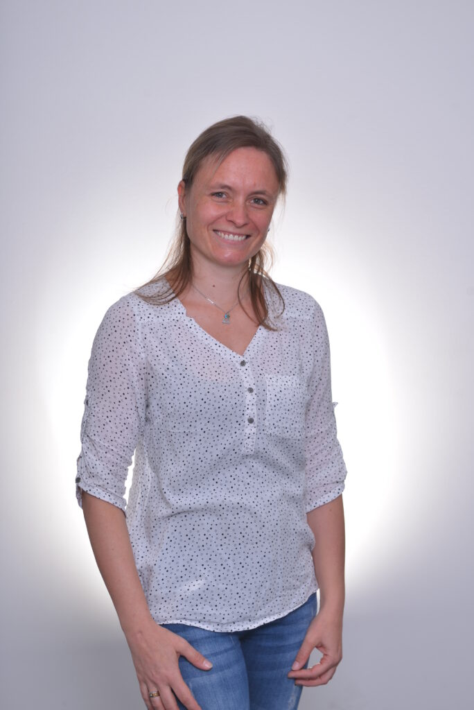 Mitarbeiterin in weißer Bluse vor neutralem Hintergrund.