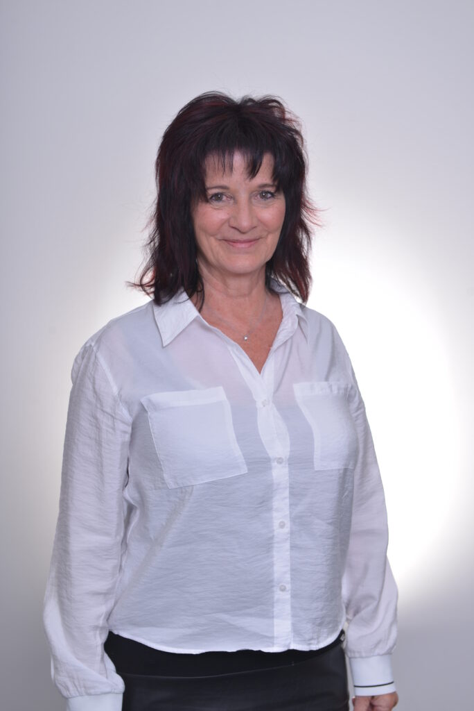 Mitarbeiterin in weißer Bluse vor neutralem Hintergrund.